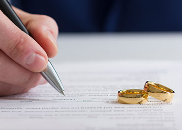  Person signing divorce papers with two gold wedding rings placed on the document